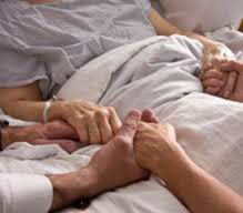 volunteers gathered around a patient's bed holding the patient's hands